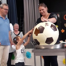 Kindergartenkind schlägt mit einem Hammer auf einen übergroßen Fußball aus Schokolade