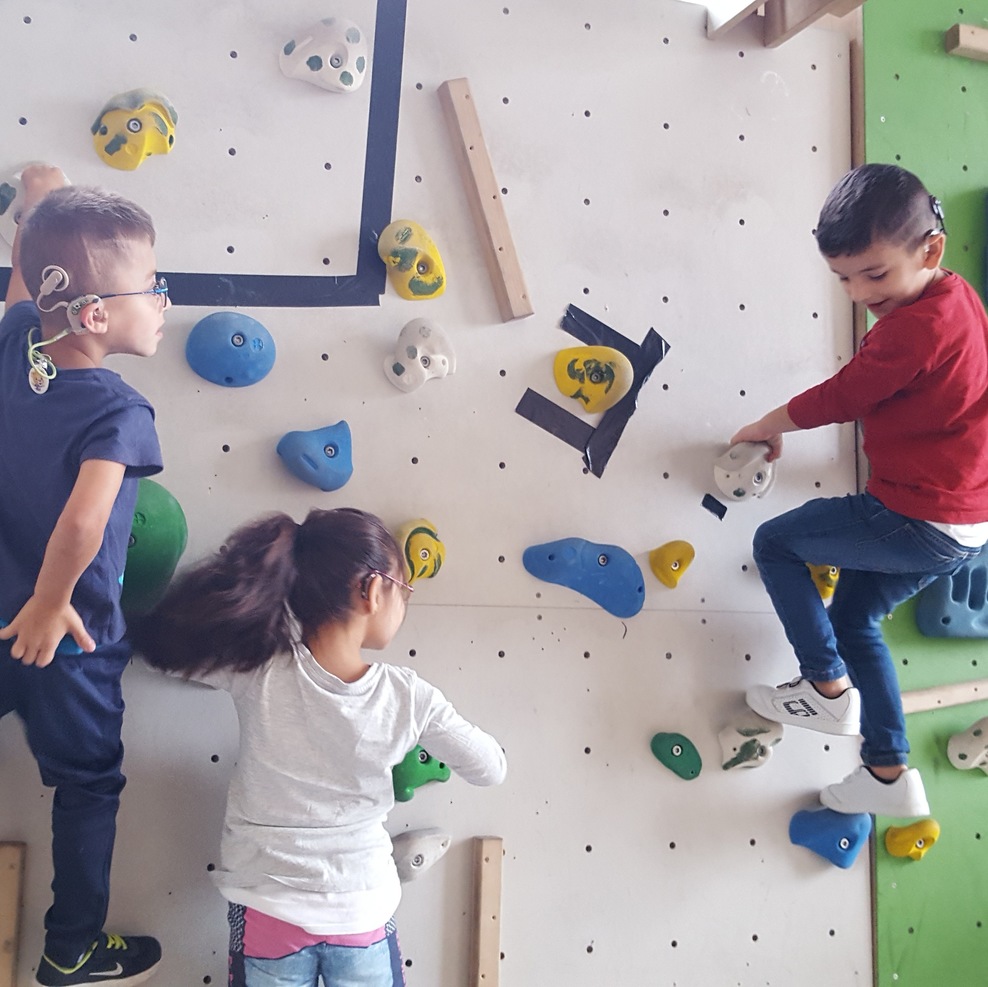 3 Kindergartenkinder klettern in einer Kletterwand